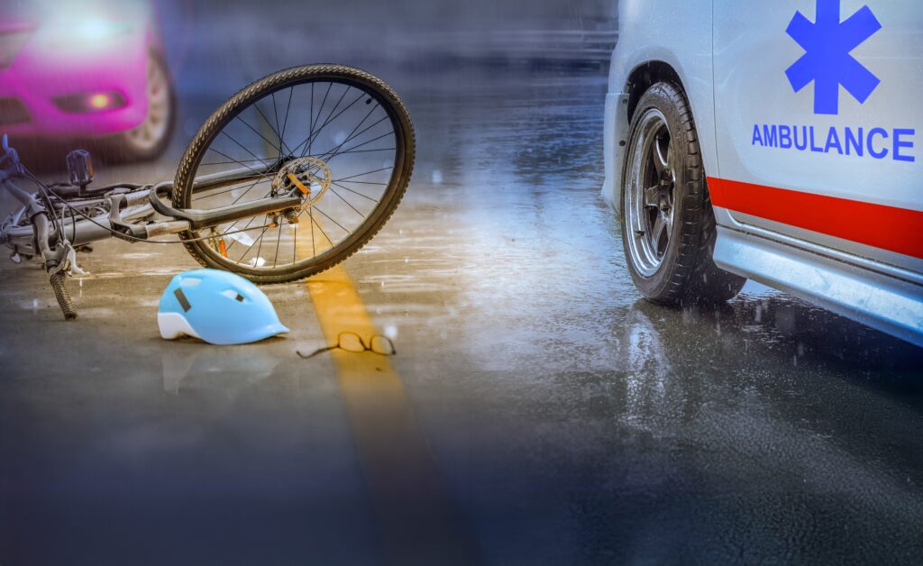Bicycle and helmet lying on a wet Detroit street beside an ambulance after a crash