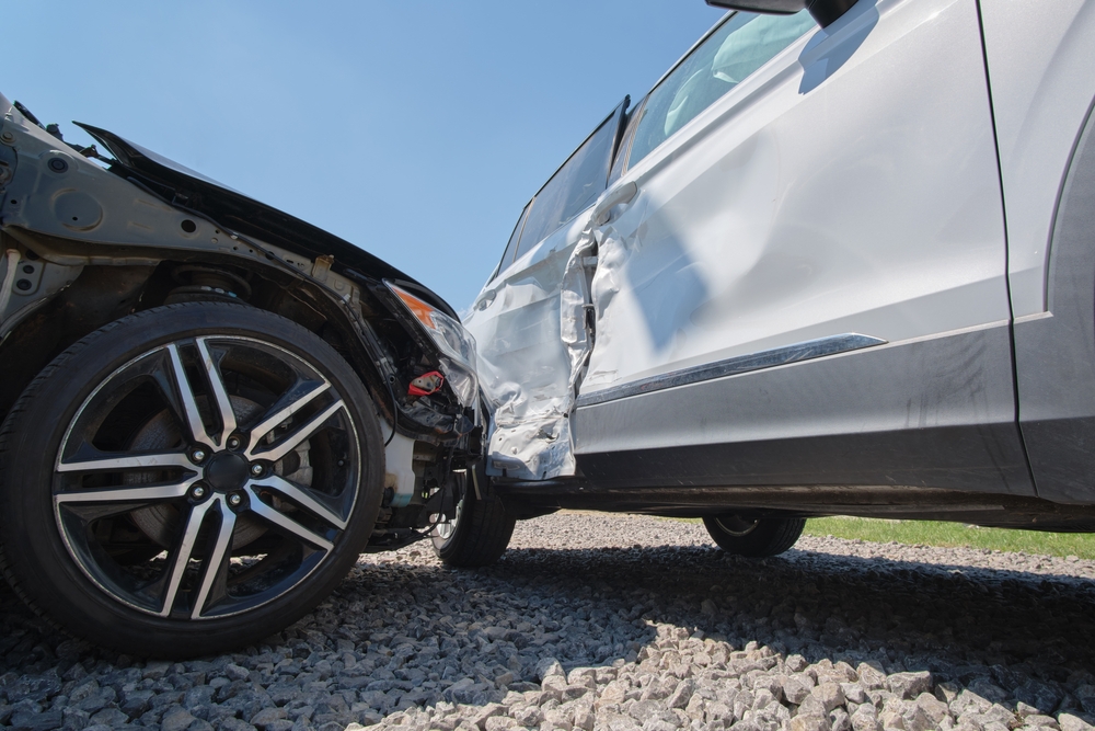 Damaged vehicles after a side-impact collision, with one car showing significant damage to the front and the other to the side door, parked on a gravel surface under a clear blue sky.