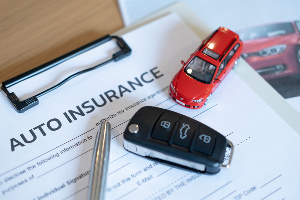 Car insurance form with a toy car, keys, and a pen, illustrating car accident claims handled by an Ann Arbor car accident lawyer.