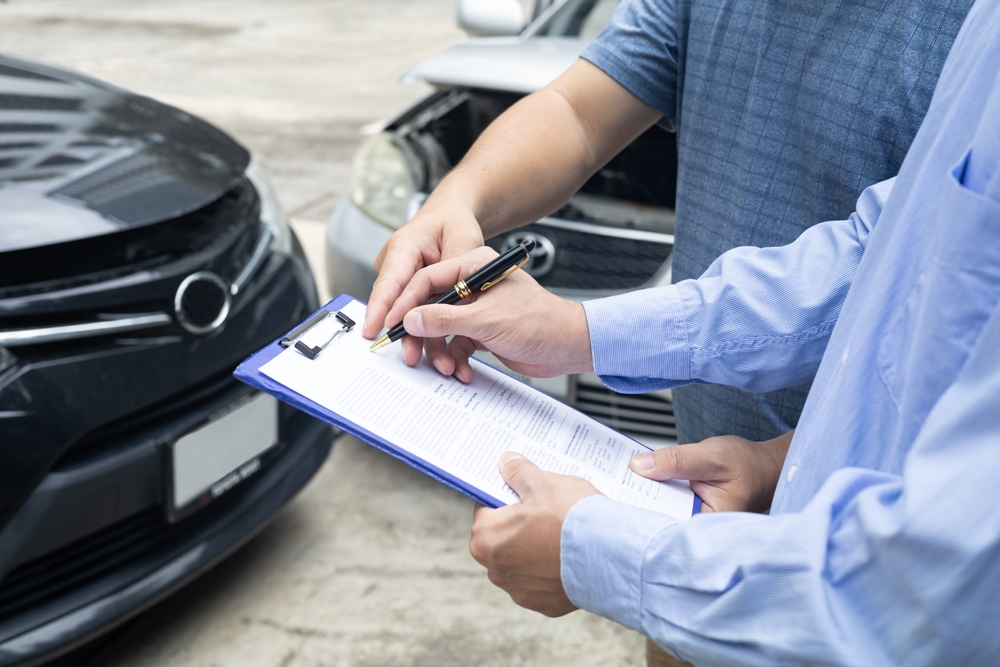 Two people reviewing an insurance form on a clipboard in front of damaged cars, illustrating car accident claims and statute of limitations deadlines.
