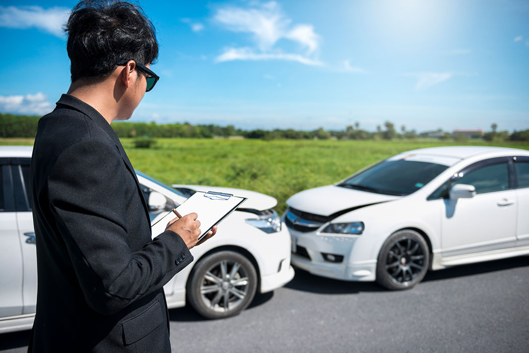 Insurance adjuster examining a damaged car with a clipboard, illustrating how car accident settlements are evaluated.