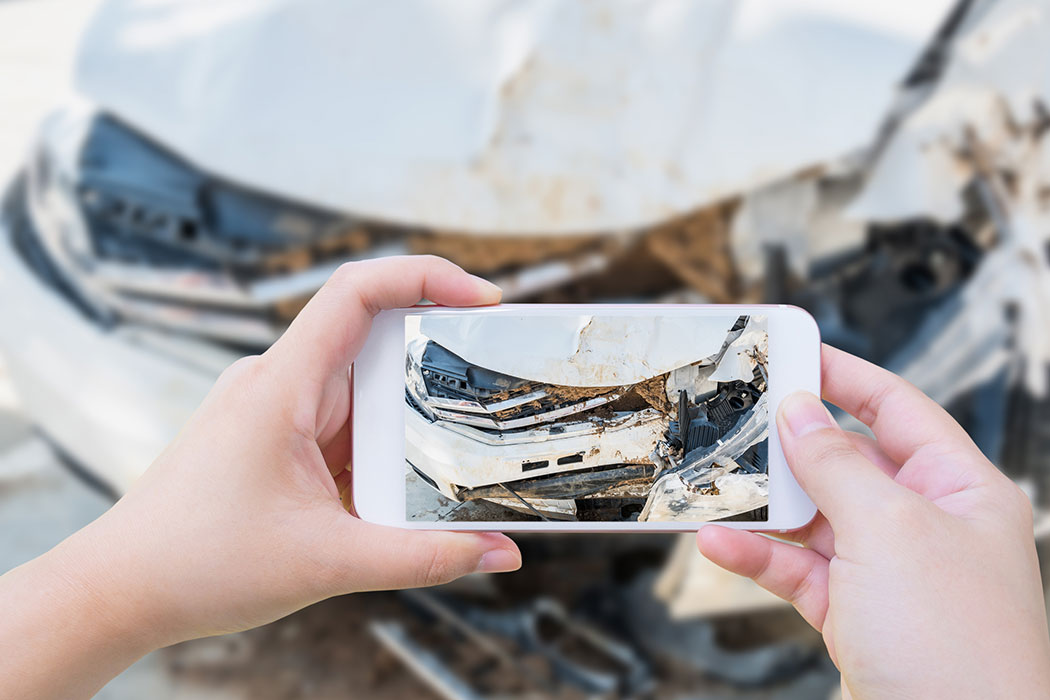 Person taking photos of car crash damage with a smartphone, showing an important step to take after a car accident in Grand Rapids.