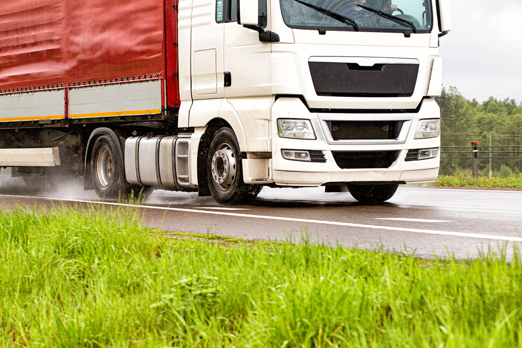 Semi-truck pulling a trailer through heavy rain on a slick roadway, representing dangerous weather-related truck accidents in Dearborn, Michigan.