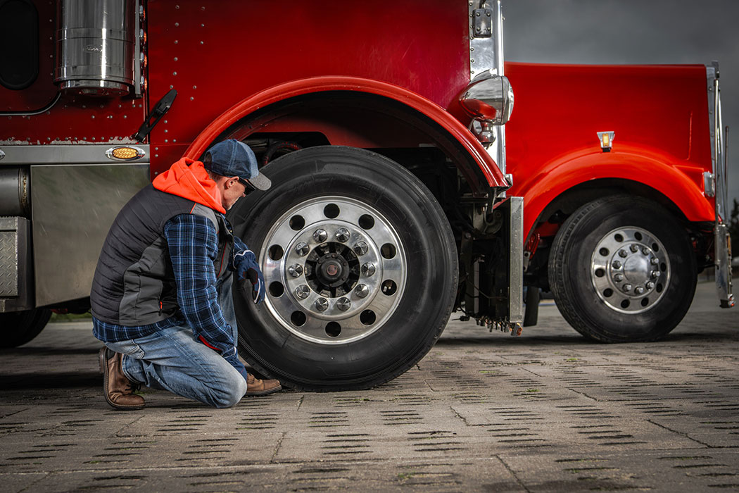 Commercial truck driver checking a trailer tire at a service stop, representing maintenance failures and liability in Dearborn truck accident claims.