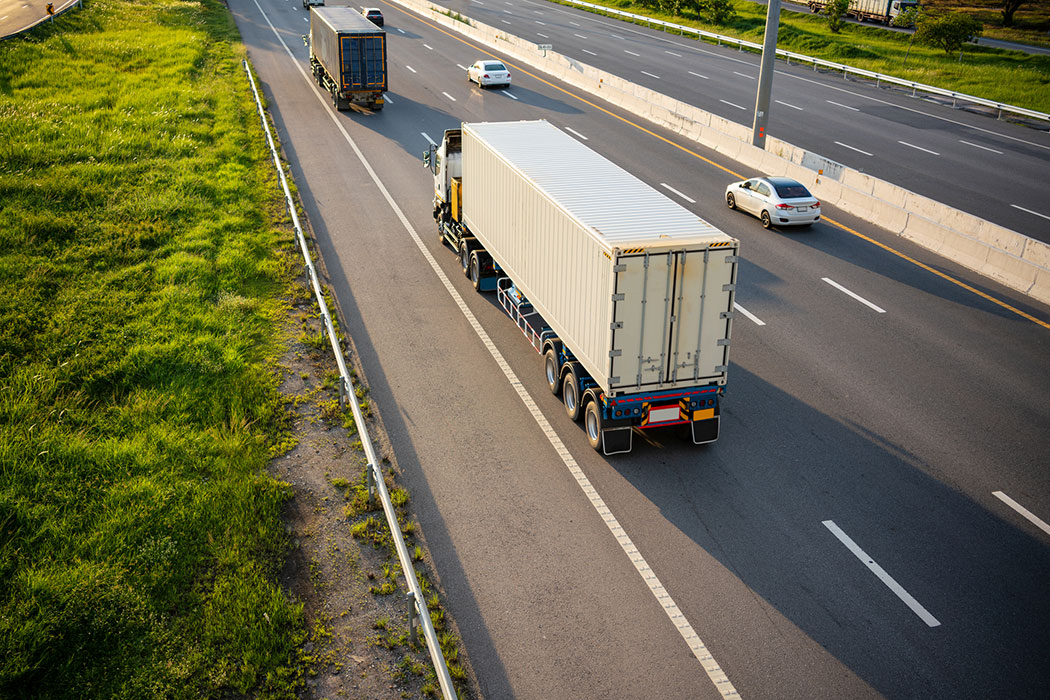 Aerial view of a white semi-truck hauling a container on a highway, showing high-volume freight movement tied to rising crash risks around Detroit’s I-75.