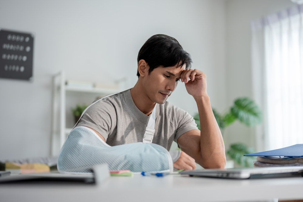 Man wearing an arm sling reviewing medical bills and expenses while recovering from injuries after an accident.