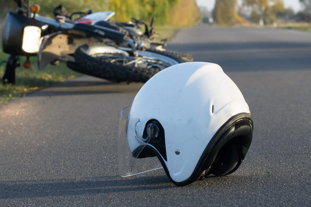 White motorcycle helmet on the road with a crashed bike in the background 