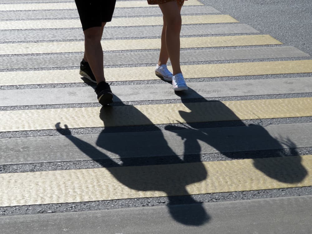 Silhouettes of pedestrians crossing a crosswalk in backlit sunlight