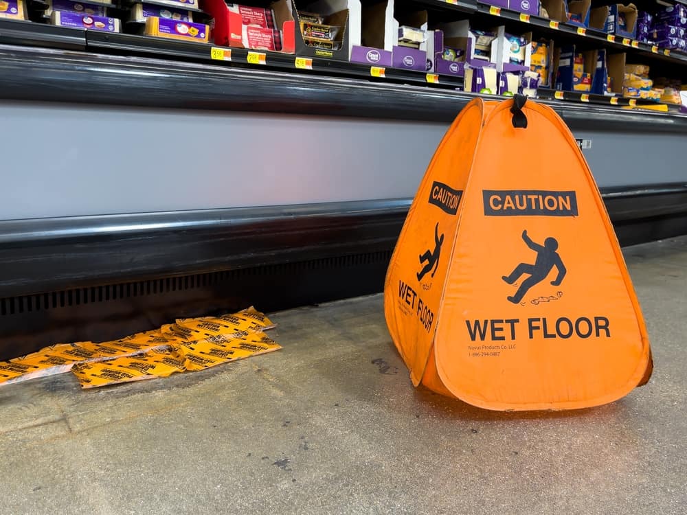 Orange caution wet floor sign in a grocery store aisle near a spill