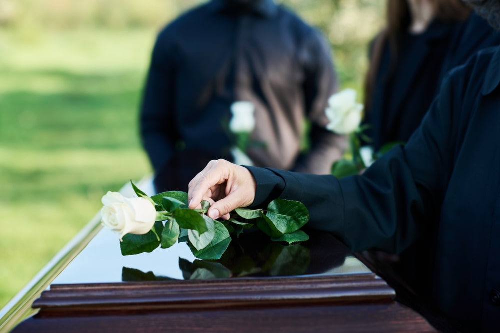 Person carrying flowers while visiting the gravesite of a loved one in a cemetery.